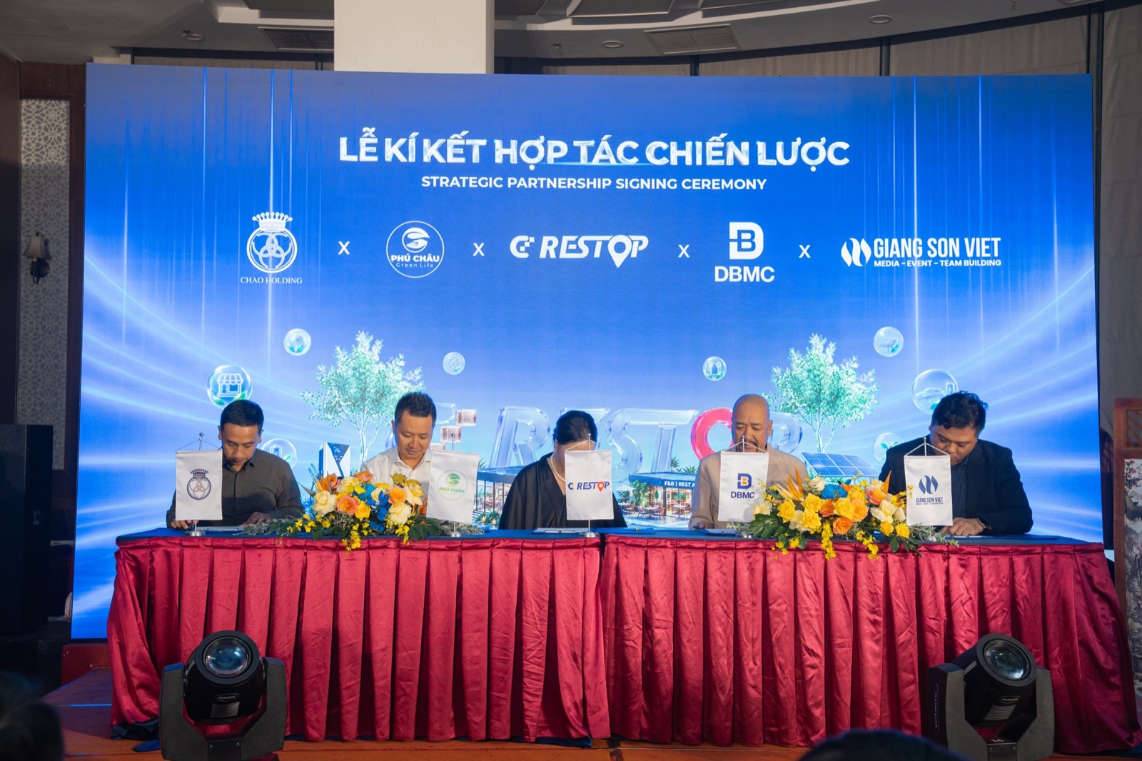 Năm đại diện ngồi ký văn kiện trên dãy bàn phủ khăn đỏ, cờ để bàn lần lượt của Chao Holding, Phú Châu, CD Restop, DBMC và Giang Sơn Việt